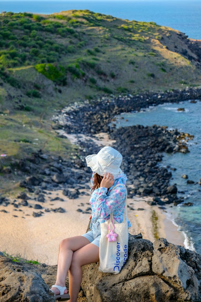 gallery-2 Woman in summer attire sitting on rocks overlooking a scenic beach view.