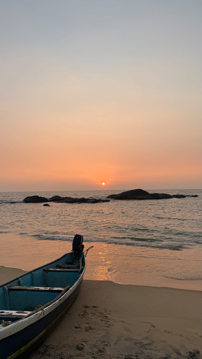 about-01 A serene sunset over a calm sea with an abandoned boat on the sandy shore, evoking peace and solitude.