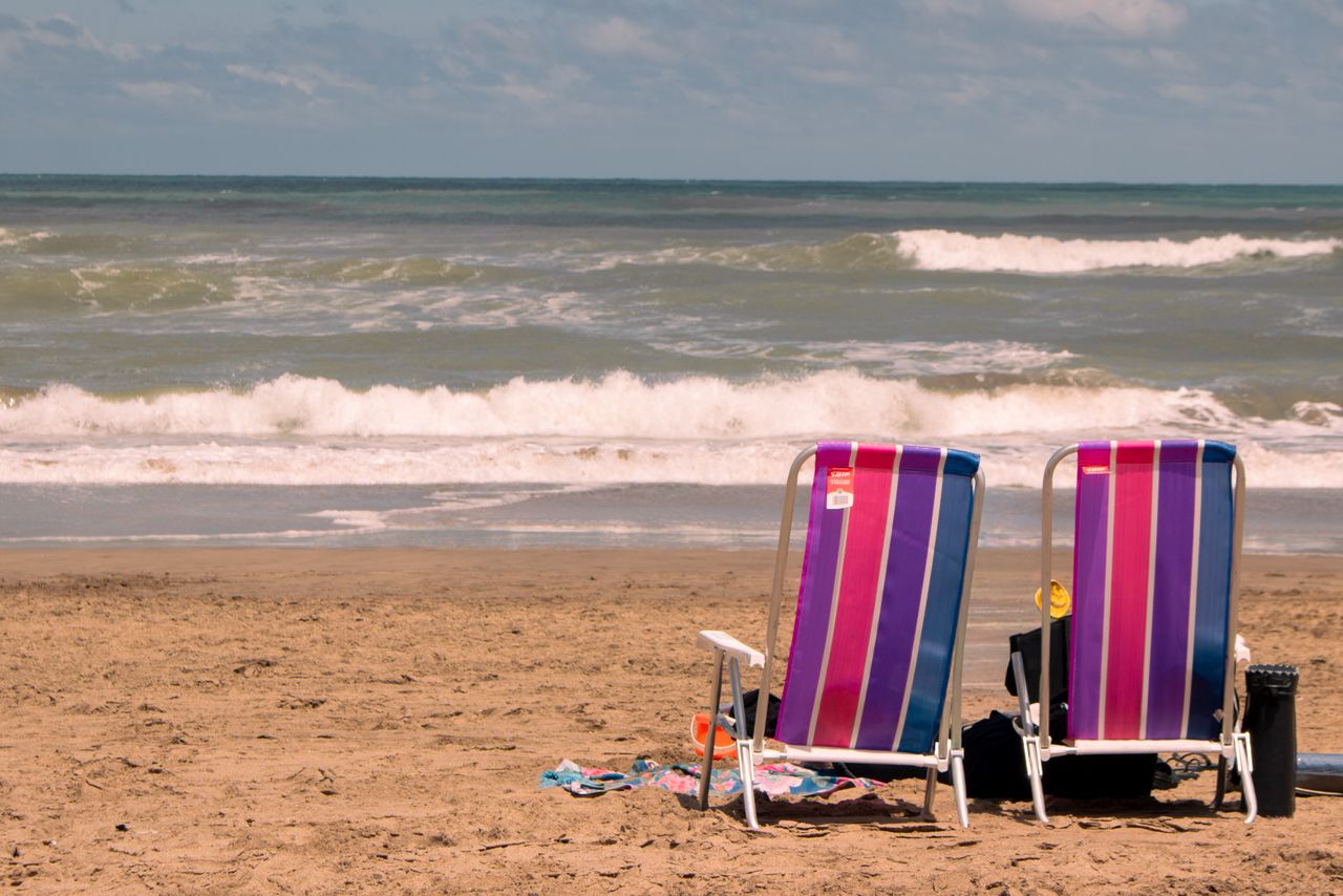 Two vibrant beach chairs facing the ocean on a sandy beach under a clear sky.