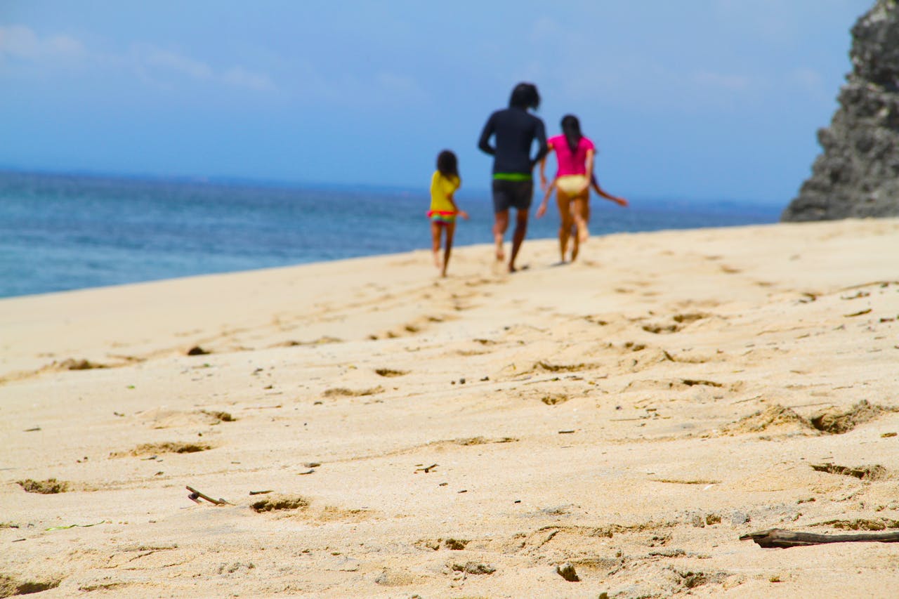 A family strolls along a sandy beach under a bright summer sky, enjoying leisure and nature.